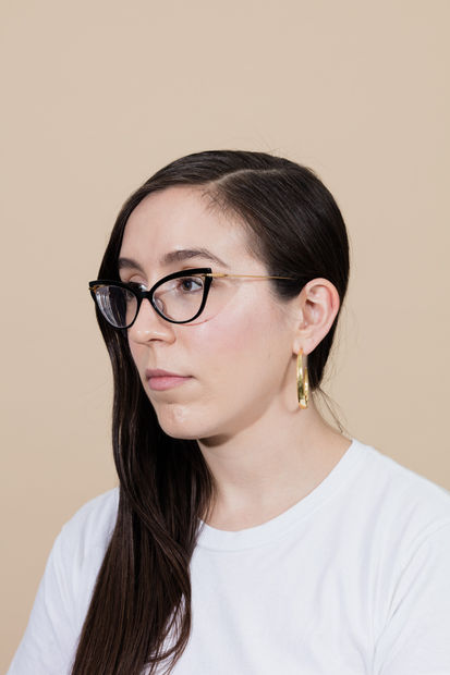 Portrait of Coady Brown who is has long brown hair to the side, cat-eyed glasses, and is wearing a white shirt.