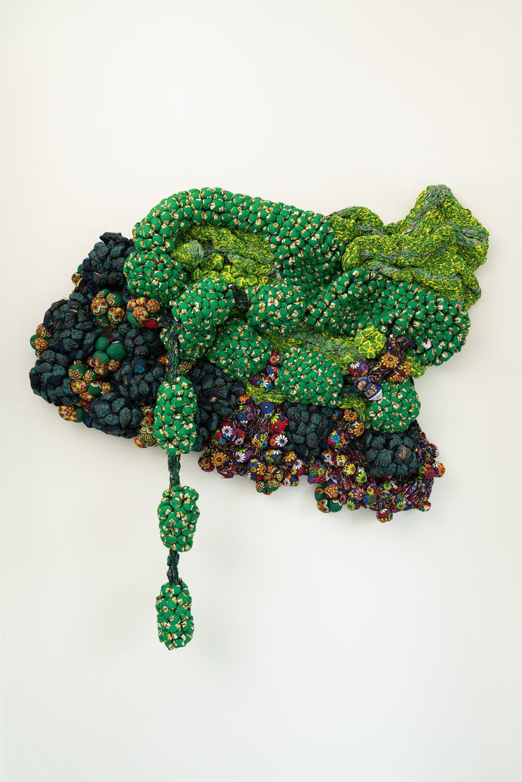 Time and Chance In a generous palette of tropical greens heightened by accents of multicolored “bubbles”, Time and Chance undeniably distinguishes itself within Samuel Nnorom’s body of work. The suspended fabric accumulations, detached from the main structure and hanging in mid-air, constitute a unique element within his artistic corpus. Through his sculpture, the artist reflects on the mutual influence of time and chance on individual lives and their impact on the social fabric of society. To convey this concept, Nnorom evokes a luxuriant forest, abundant with vibrant flowers and succulent fruits, blessed by the passage of time and the fortuitous elements of chance.