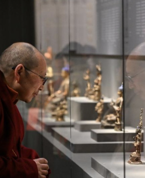 Tibetan monk looking at sculptures in a museum vitrine