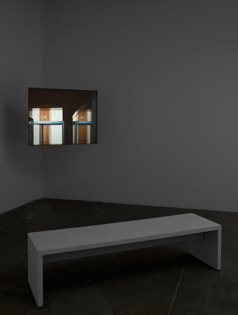 A white bench sits in front of a small screen displaying two doors illuminated by rays of light. 