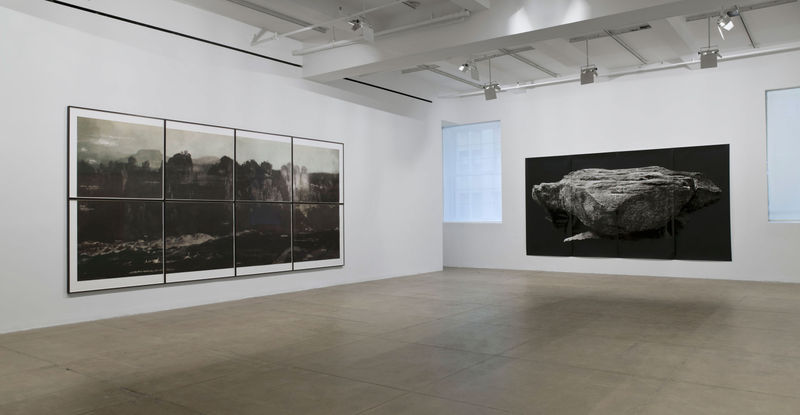 On the left wall, eight framed prints are arranged to form a landscape. A large black print of a rock against a black background hangs on the right. 