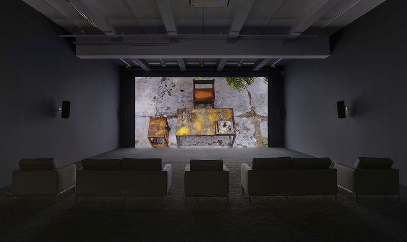 Various couches sit in front of a projection of a wooden table and chair in an outdoor setting. 