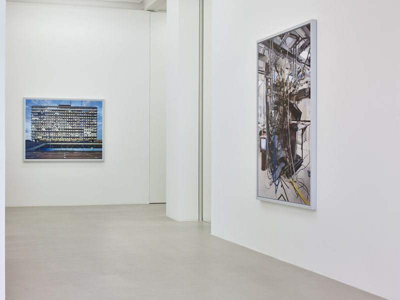 On the far, straight-on wall, a photograph hangs of giant office building. On the near right wall, a photograph hangs of machinery building an unidentified object.