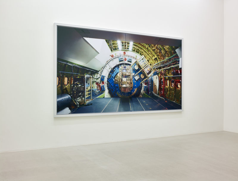 On a white wall, a large rectangular photo, framed in white, shows the interior of what appears to be a spaceship - heavy gold, blue, and white machinery.