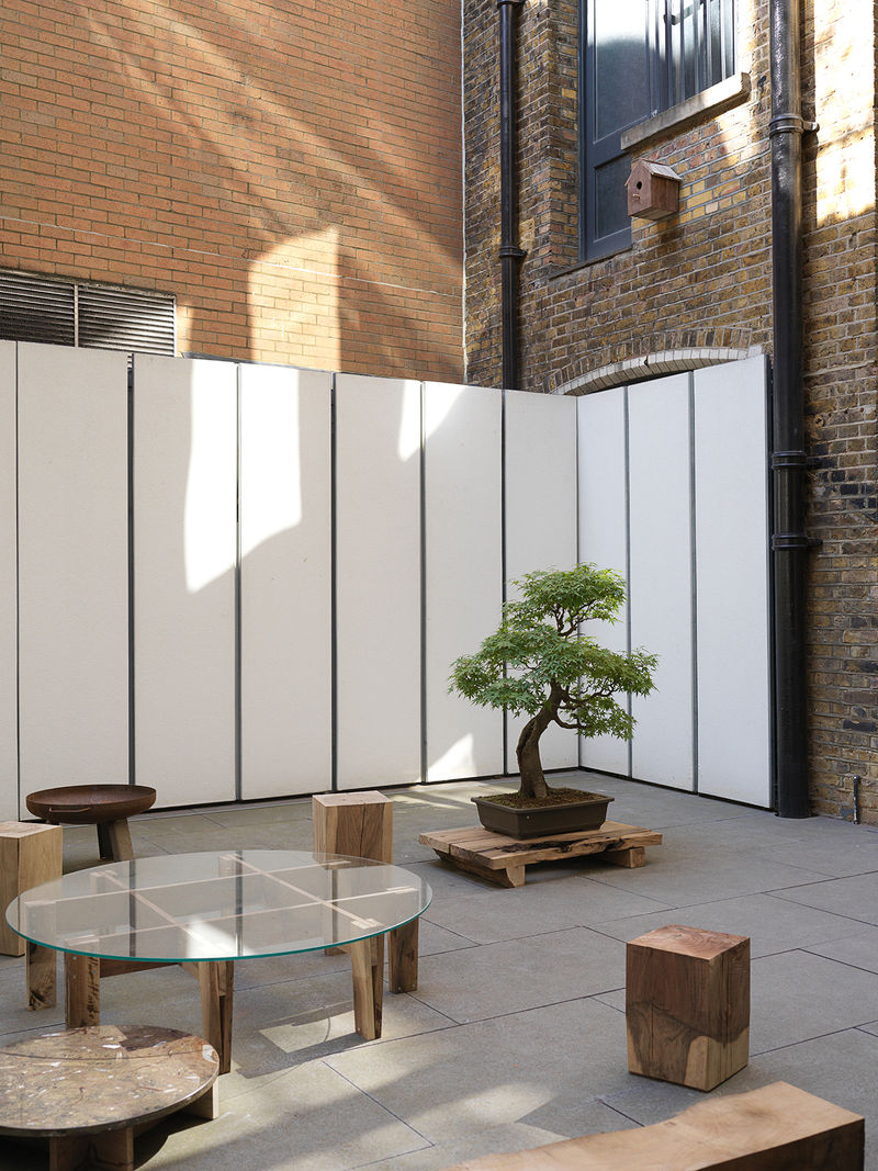 Outdoor gallery filled with assorted wood and glass furniture and a bonsai tree.
