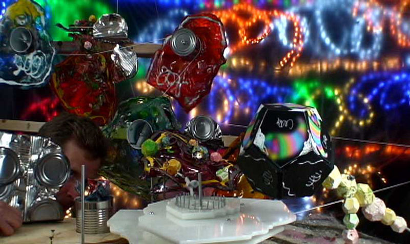 Man peeks out of multi-colored sculpture with many mechanical elements