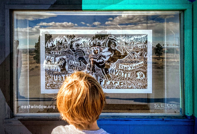 The back of a child's head as he views the Sue Coe linocut "We are Many. They are Few" in the window of East Window Gallery, Boulder, CO. 