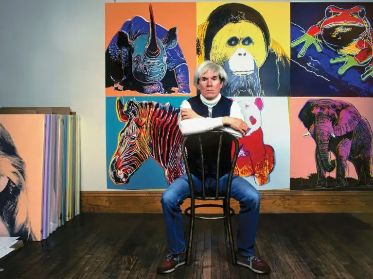 Andy Warhol sitting in front of his colorful animal artwork collection