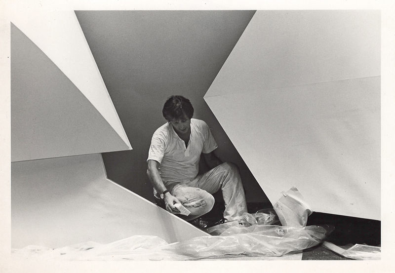 Charles Hinman kneeling between two abstract shaped canvas paintings