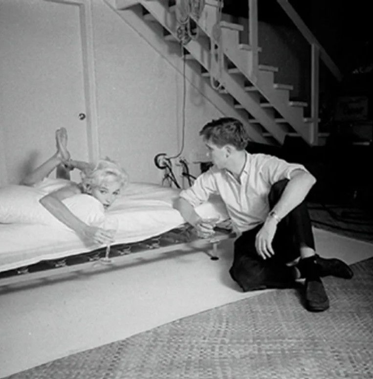 black and white photograph of Marilyn Monroe lying on her stomach in bed speaking to photographer Douglas Kirkland