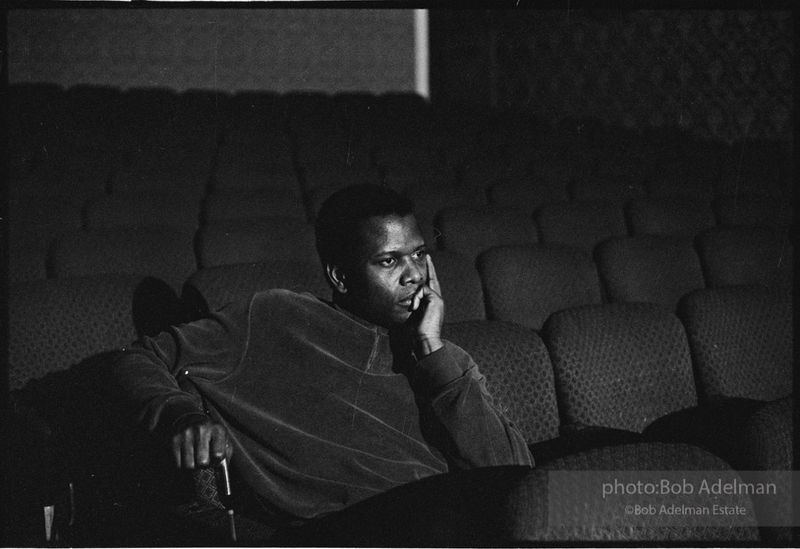 Sidney Poitier holds his head sitting in a theater-like setting