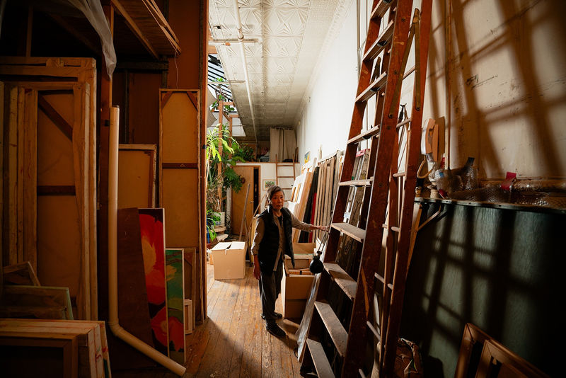 Photograph of an artist standing amongst canvases in a loft setting