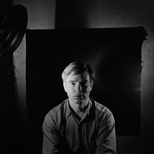 black and white photograph of Andy Warhol illuminated from either side with studio lighting
