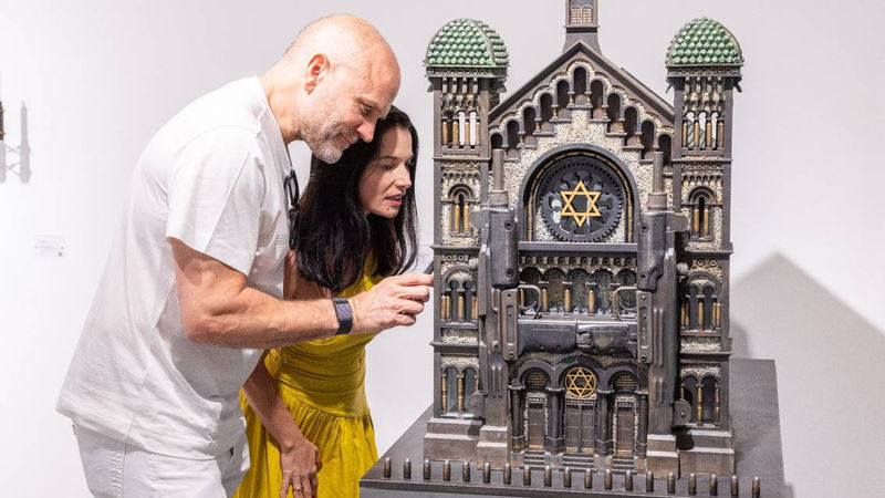 Guests look into a sculpture of a synagogue by artist Al Farrow at VISU Contemporary in South Beach. SHOT BY SHAUN PHOTOGRAPHY Read more at: https://www.miamiherald.com/entertainment/visual-arts/article287924125.html#storylink=cpy