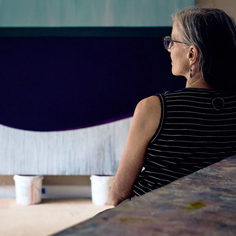 Photograph of artist Sarah Hinckley at her Cape Cod painting studio, sitting with one of her large oil on canvases.