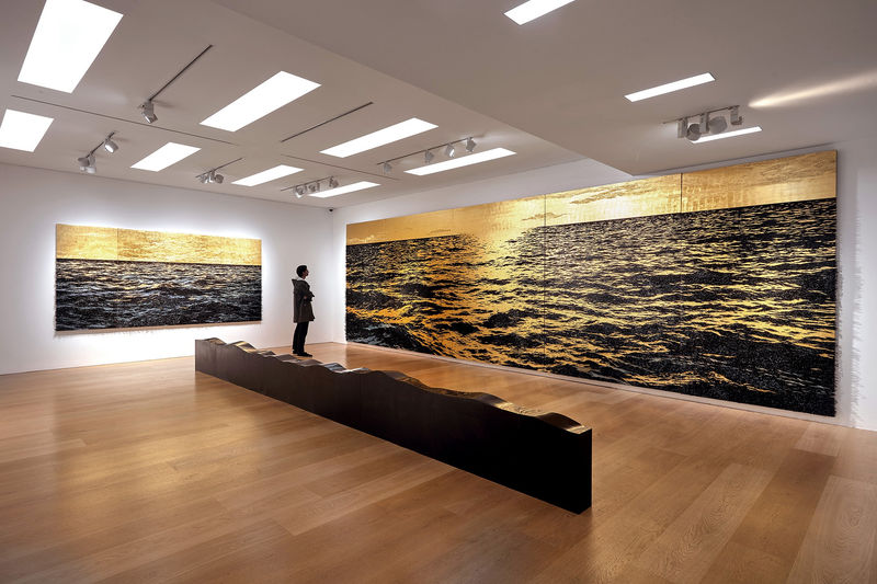 Installation view of a white cube gallery showing an exhibition by Yoan Capote - the works are large canvases that are covered in gold leaf and black fishhooks