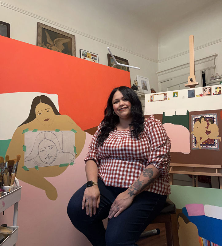 portrait of Gina M. Contreras - woman in plaid shirt sitting in front of her paintings on easels of nude women