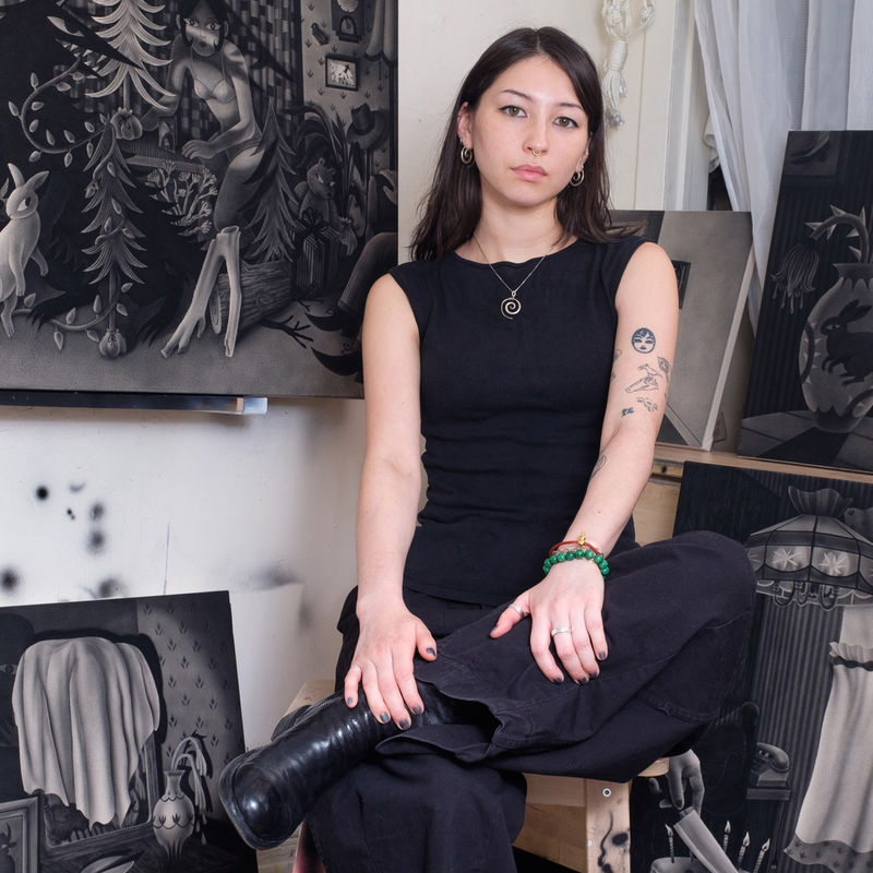 Angela Fang Zirbes portrait - woman in her studio wearing all black. Monochromatic paintings (b&w) in background