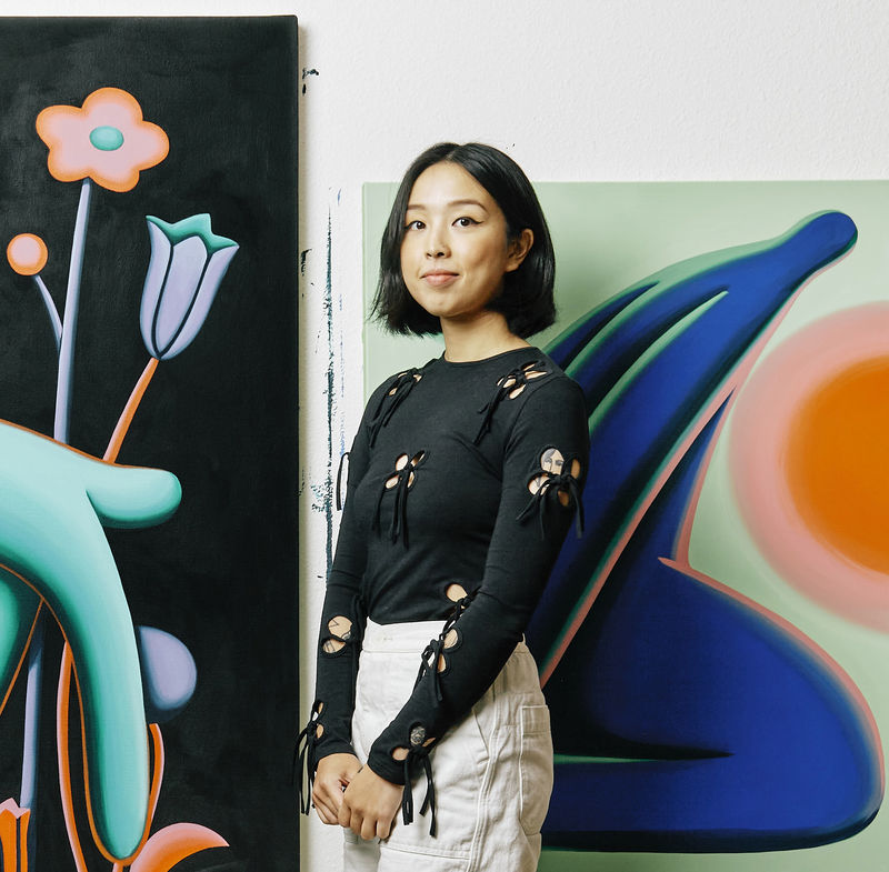 photograph of Artist Jocelyn Tsaih standing in her studio next to her paintings
