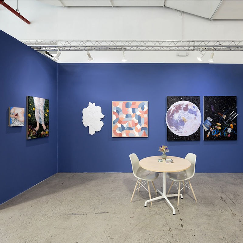 blue booth with various artworks hanging on walls. round table to the right