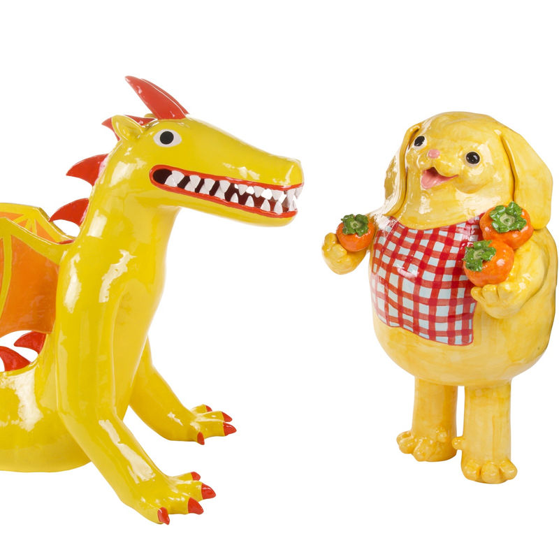 bright yellow and orange dragon next to a bright yellow dog holding persimmons