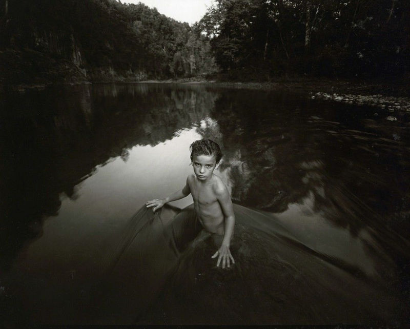 Sally Mann Immediate Family The Last Time Emmett Modeled Nude, portrait of son Emmett nude in river with hands touching water's surface trees in background