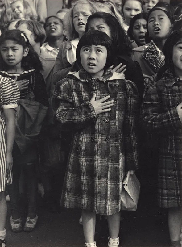Japanese American schoolgirl amongst classmates of different races saying the pledge of allegiance with her hand on her chest