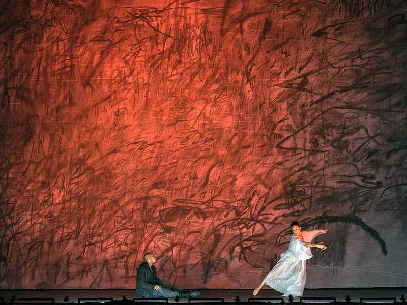 Two people dancing on stage in front of dark red background.