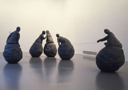 Figure-like sculptures with rounded spheres instead of legs interact with one another.