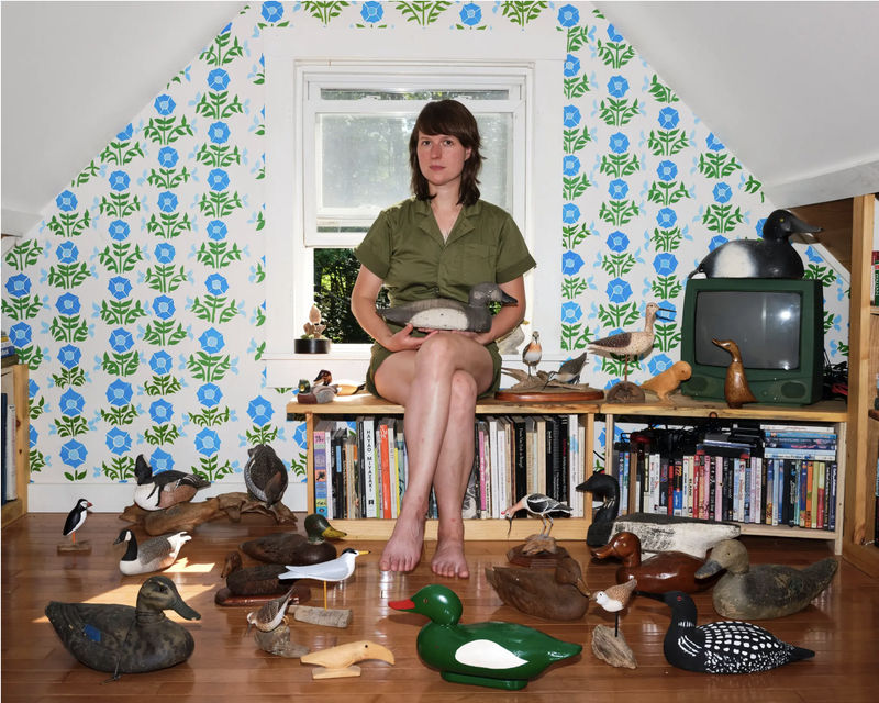 The artist Anne Buckwalter at her home in Durham, Maine, with hand-carved wooden bird decoys from her collection. She hand-painted the mural on the wall behind her.
