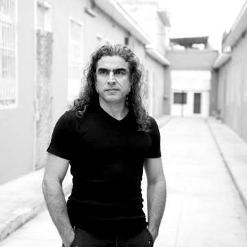 Black and white photograph of a light-skinned man with a black t-shirt and long, greying hair that falls across his shoulders. He is looking intently off to the left of the photo.