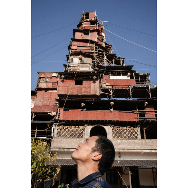 2024年2月，贵州兴义市，陈天明与他的“移动城堡”的合影。“2018年，我从江浙地区回老家后就开始建造，算是自然而然，多次拼凑尝试、逐渐组合而成，也有一点艺术冒险性，有好奇心，探索木结构建筑，为了稳固逐层减小而呈塔状。最近五年开荒复垦务农，2020年开始养土鸡土鸭，2021年逐渐种草养鹅养牛，其实养殖都亏损，2023年下半年开始卖牧草，未来的计划是减少养殖。”——来自他的自述  February 2024, Xingyi, Guizhou Province Chen Tianming and his 