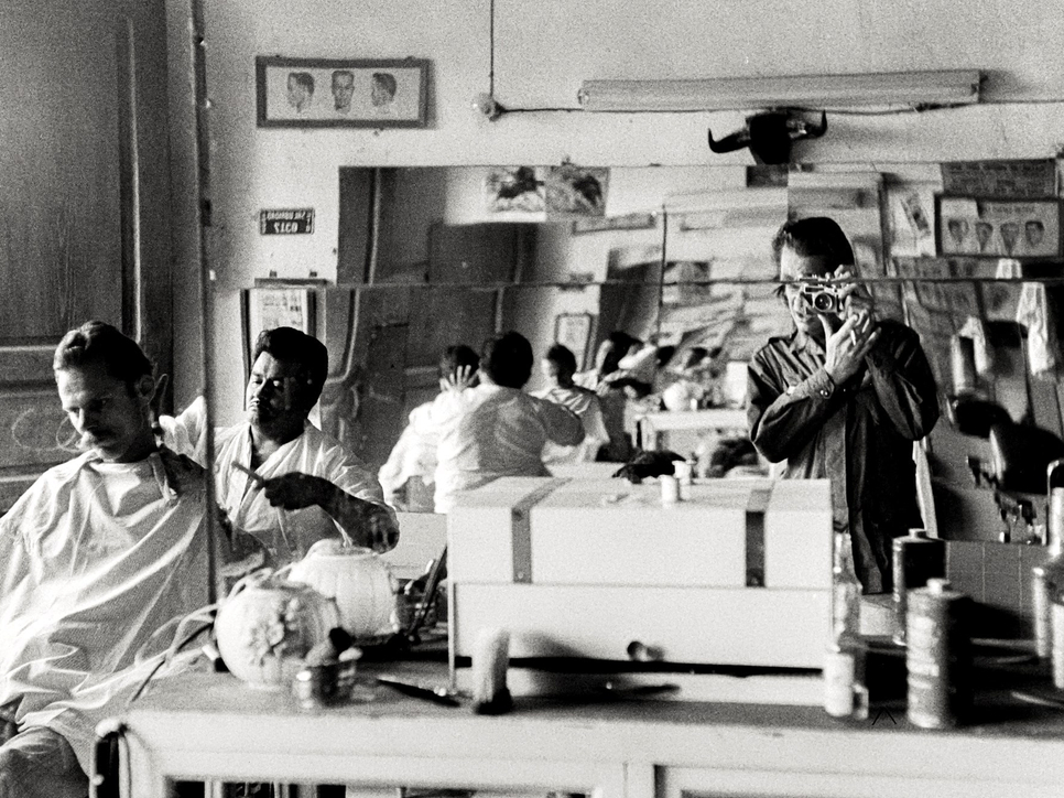 Black and white photo of a photographer taking a picture in the reflection of a mirror in a barber shop